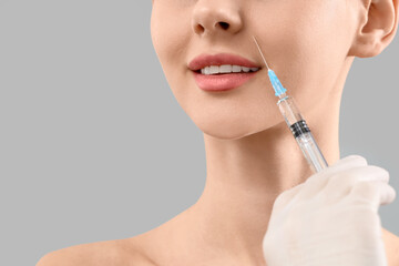 Young girl receiving filler injection in face against grey background, closeup