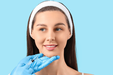 Young girl receiving filler injection in lips on blue background