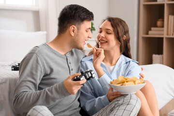 Young couple with potato chips playing video game in bedroom