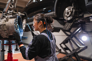 Female chinese mechanic inspecting car part in repair shop