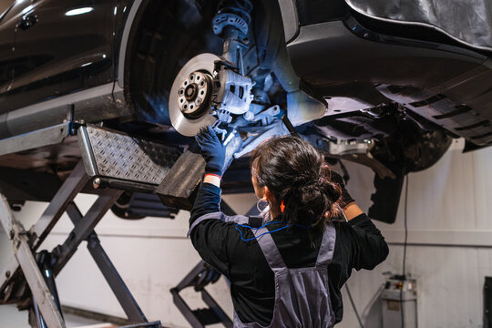Female mechanic working under a car on a lift in a repair shop