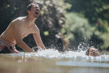 Fototapeta premium A joyful father and child splashing in a sunlit natural body of water. The scene captures laughter, bonding, and the fun of outdoor activity in a refreshing setting.