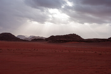 A desert landscape with a cloudy sky and mountains in the background