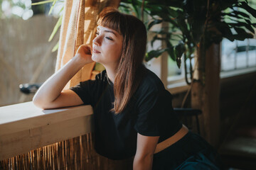 A thoughtful woman gazes outside while sitting by a window, enveloped in soft natural light and surrounded by indoor plants. The scene evokes a sense of contemplation and tranquility.