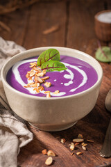 A bowl of creamy purple beet soup topped with a swirl of cream, toasted almonds, and fresh herbs, resting on a rustic wooden board.