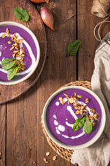 Red cabbage soup decorated with vegetables and pieces of toasted almonds on a rustic wooden board, accompanied by a spoon and shallots, creating a visually attractive and appetizing setting. Top view