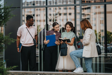 A diverse group of young business people engaged in a collaborative outdoor meeting. They are sharing notes and discussing ideas in a modern urban setting.