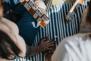 A close-up of friends playing a board game with rummikub tiles on a striped blanket, capturing a moment of togetherness, relaxation, and friendship.