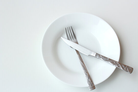 Empty plate with crossed cutlery symbolizing lack of food or malnutrition concept. International hunger day on May 28th. Diet, hungry, meal, starvation theme.