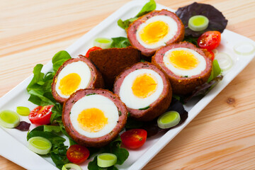 Meat stuffed eggs (Scotch egg) served with cherry tomatoes and greens - Scottish food