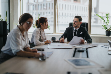 A group of diverse business people in a modern office setting, discussing documents during a collaborative meeting. The atmosphere is focused and professional, reflecting teamwork and communication.
