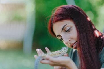 A young woman gently holds a lizard in her hands, showcasing curiosity and fascination in a serene garden setting, with lush greenery as the backdrop.