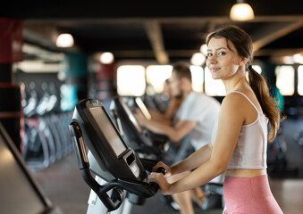Fototapeta premium Young woman in sportswear training on exercise bike in gym