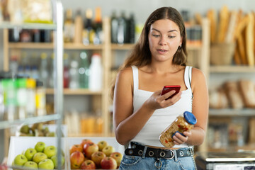 Female customer scans QR code on beans jar label using smartphone. Checking products in a supermarket