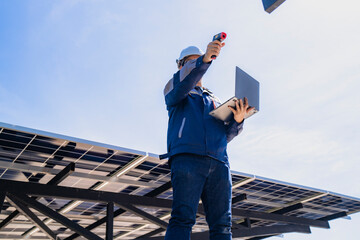 Engineer inspecting solar panels using infrared equipment while holding a laptop under a clear blue...