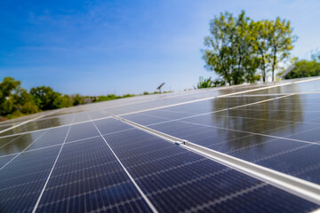 Close up view of solar panels installed on a carport with trees and parked cars under a clear blue...