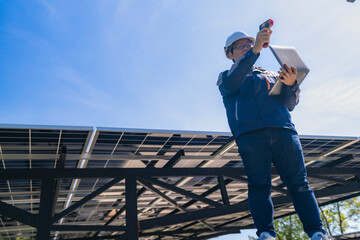 Engineer inspecting solar panels using infrared equipment while holding a laptop under a clear blue...