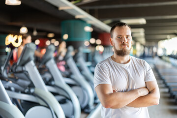 Fototapeta premium Young guy trainer in sportswear poses in middle of fitness center gym. Active lifestyle, daily workouts in crossfit gym