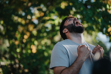 A bearded man celebrates with enthusiasm amidst lush greenery, showcasing intense emotion and joy. The vivid background adds a dynamic feel to the scene, highlighting his exhilaration and victorious
