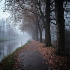 Obraz premium Misty path lined with trees, beside still canal on an autumn day.