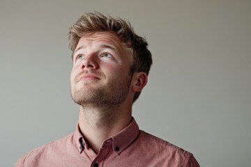 Obraz premium Thoughtful Young Man Gazing Upwards with Hopeful Expression in a Minimalistic Setting