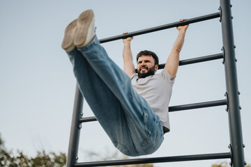 Obraz premium A man demonstrates strength and fitness by hanging from a pull-up bar outdoors. His expression shows determination and focus, showcasing an active lifestyle and a dedication to physical health.