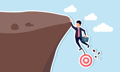 A businessman is at risk of falling while holding onto a target board at the edge of a cliff, illustration of facing failure in meeting company business targets
