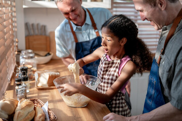 Caucasian senior gay couple baking bakery with adopted daughter in house. 