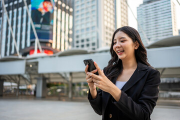 Asian young businesswoman using smartphone while standing in the city. 