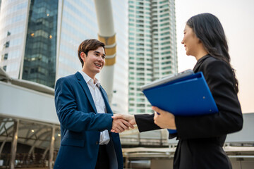 Asian businessman and woman making handshake outdoors in the city. 
