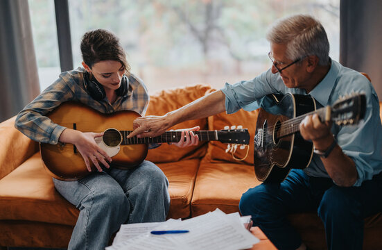 An elderly professor guides a student in playing the guitar during a music class. The lesson takes place in a relaxed school setting, fostering learning and creative expression. - Powered by Adobe
