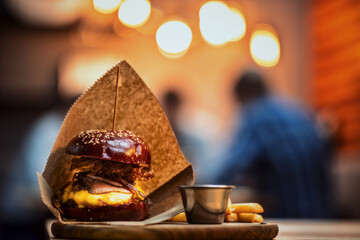 A gourmet cheeseburger with a pretzel bun, crispy fries, and sauce served on a rustic wooden board in a cozy dining ambiance.