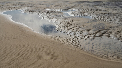 The time of low tide in the ocean. Puddles formed on the exposed wavy sand. The sky is reflected in the water. Close-up. Madagascar. Morondava