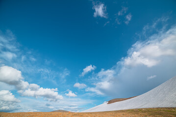 Orange tent on stony mountain pass in bright sun. Glacier on stone hillside under clouds in blue sky. Rock hill with snow on high altitude in sunny day. Rocky snowy mountainside in changeable weather.