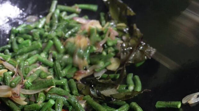 Oseng or tumis buncis daun salam bawang putih is being cooked in a black wok. The saut&eacute;ed green beans, garlic, and bay leaves, sizzling. Indonesian javenese dish. Homemade delicious flavorful stir fry