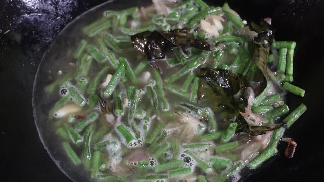 Oseng or tumis buncis daun salam bawang putih is being cooked in a black wok. The saut&eacute;ed green beans, garlic, and bay leaves, sizzling. Indonesian javenese dish. Homemade delicious flavorful stir fry