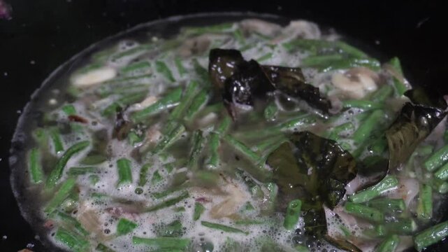 Oseng or tumis buncis daun salam bawang putih is being cooked in a black wok. The saut&eacute;ed green beans, garlic, and bay leaves, sizzling. Indonesian javenese dish. Homemade delicious flavorful stir fry