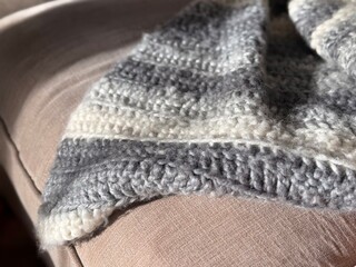 A soft and warm knitted blanket in shades of gray and white, resting on a couch and illuminated by natural light, evoking feelings of coziness and comfort.