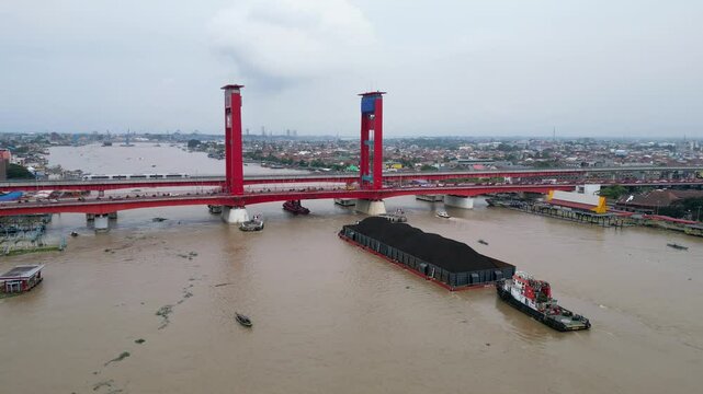 Barges carrying coal pass the Ampera Bridge on the Musi River