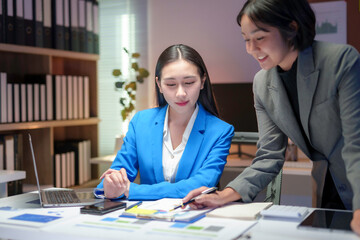 Two asian businesswomen are working late in the office, discussing a financial report together in a meeting room