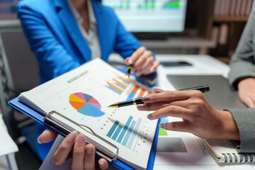 Businesswomen are pointing at charts and graphs on a clipboard, analyzing financial data and developing growth strategies