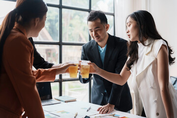Asian business colleagues toasting with drinks, celebrating a successful project or achievement in a modern office environment