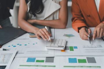 Businesswomen working together, analyzing financial charts, using calculator, discussing data, and collaborating on a project in a modern office