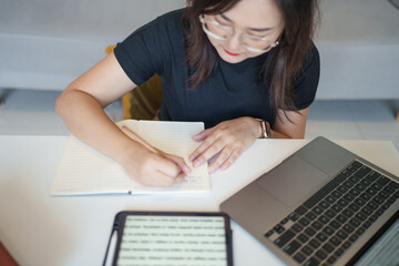 Asian woman using pencil writing on notebook in living room