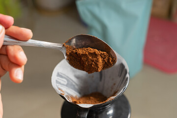 Close-up of a spoon filled with ground arabica coffee above a V60 coffee filter in a pour-over dripper. Showcases the V60 brewing process, fresh coffee preparation, and aromatic manual coffee-making.