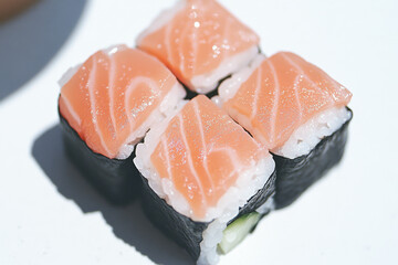 A sushi roll with four pieces of salmon and a cucumber