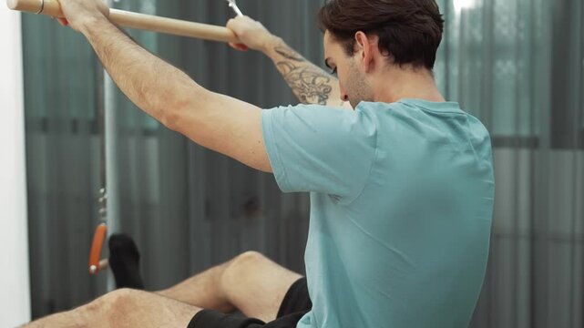 Man performing seated core exercise on pilates trapeze holding bar to strengthen arms and core muscles at gym. Trainer doing chest press on the cadillac for strengthening chest, shoulder. Habituate.