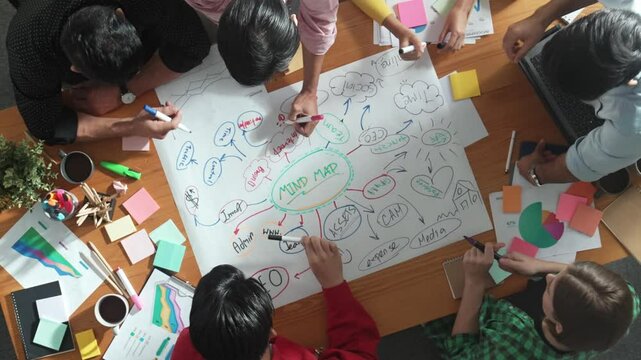 Group of business people writing and making mind map to brainstorming marketing idea at meeting. Top aerial view of investors sharing plan or strategy by using sticky notes and marker. Convocation.
