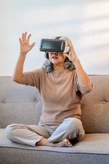 Excited mature woman wearing virtual reality goggles at home.