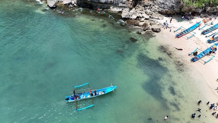 aerial view of white sandy beach in tropical island. people enjoying vacation in tropics. blue fishing boat by the beach.